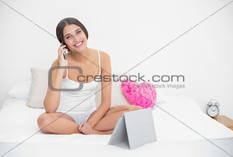 Delighted young brown haired model in white pajamas making a phone call