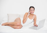 Charming young brown haired model in white pajamas making a phone call