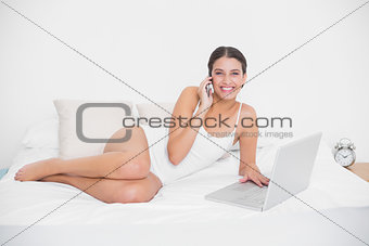 Attractive young brown haired model in white pajamas making a phone call
