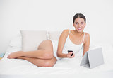 Pretty young brown haired model in white pajamas holding a mobile phone