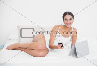 Pretty young brown haired model in white pajamas holding a mobile phone