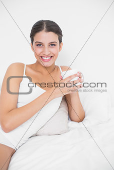 Smiling young brown haired model in white pajamas drinking coffee
