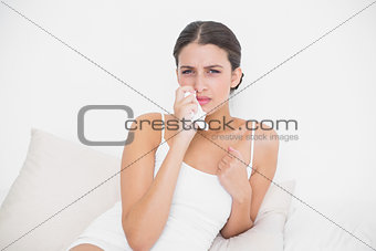 Upset young brown haired model in white pajamas wiping her eyes with a tissue