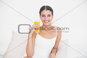 Dynamic young brown haired model in white pajamas holding a glass of orange juice