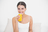 Pretty young brown haired model in white pajamas drinking orange juice