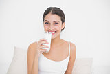 Charming young brown haired model in white pajamas drinking milk