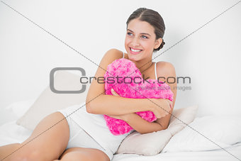 Cute young brown haired model in white pajamas hugging a heart-shaped pillow