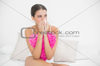 Depressed young brown haired model in white pajamas crying in a tissue