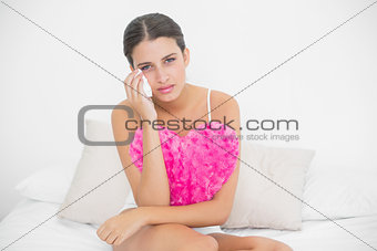 Stern young brown haired model in white pajamas wiping her tears