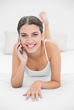 Casual young brown haired model in white pajamas making a phone call