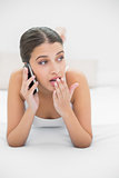 Shocked young brown haired model in white pajamas calling with her mobile phone