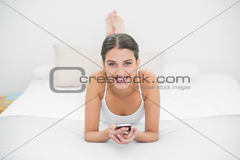 Gorgeous young brown haired model in white pajamas using a mobile phone