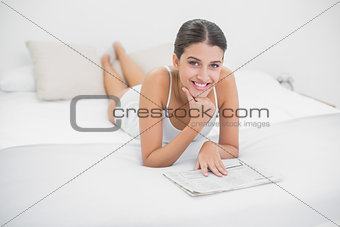 Relaxed young brown haired model in white pajamas reading a newspaper