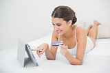 Casual young brown haired model in white pajamas shopping online with her tablet pc