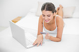 Dreamy young brown haired model in white pajamas shopping online with her laptop