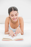 Attentive young brown haired model in white pajamas reading a book