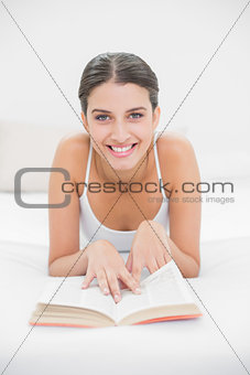 Casual young brown haired model in white pajamas reading a book