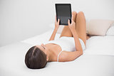 Relaxed young brown haired model in white pajamas using a tablet pc
