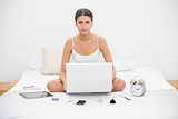 Irritated young brown haired model in white pajamas holding a laptop