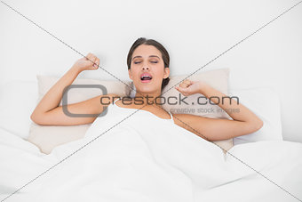 Exhausted young brown haired model in white pajamas stretching her arms