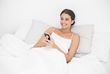 Beautiful young brown haired model in white pajamas texting with a mobile phone