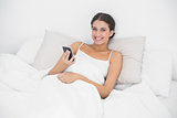 Relaxed young brown haired model in white pajamas using a mobile phone
