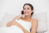Pensive young brown haired model in white pajamas making a phone call