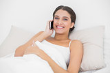 Content young brown haired model in white pajamas making a phone call