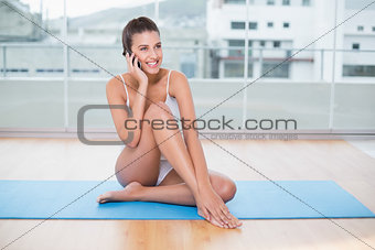 Amused natural brown haired woman in white sportswear making a phone call