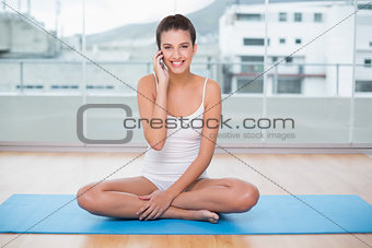 Pretty natural brown haired woman in white sportswear making a phone call