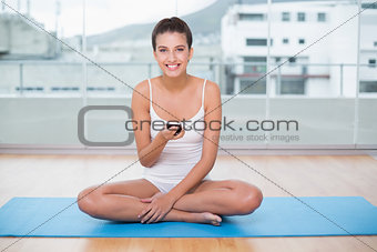 Joyful natural brown haired woman in white sportswear texting with her mobile phone