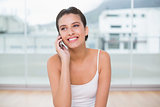 Smiling natural brown haired woman in white sportswear making a phone call