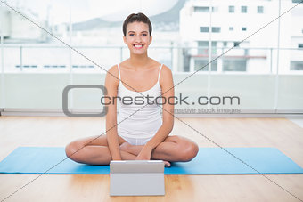 Smiling natural brown haired woman in white sportswear using a tablet pc