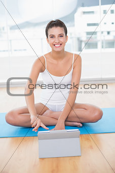 Cheerful natural brown haired woman in white sportswear using a tablet pc
