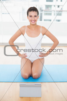 Cute natural brown haired woman in white sportswear posing with hands on the hips