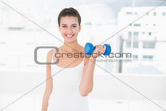 Dynamic natural brown haired woman in white sportswear lifting a dumbbell
