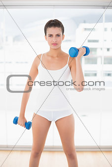 Serious natural brown haired woman in white sportswear exercising with dumbbells