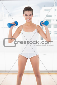Happy natural brown haired woman in white sportswear exercising with dumbbells