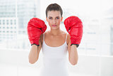 Stern natural brown haired woman in white sportswear wearing boxing gloves