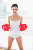 Unsmiling natural brown haired woman in white sportswear wearing boxing gloves