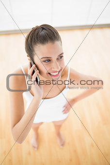 Cheerful natural brown haired woman in white sportswear making a phone call