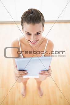 Charming natural brown haired woman in white sportswear using a tablet pc