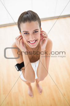 Delighted natural brown haired woman in white sportswear adjusting her earphones