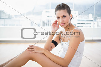 Stern natural brown haired woman in white sportswear listening to music