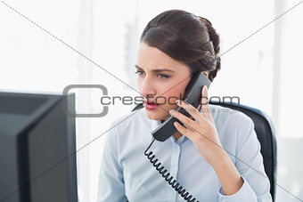 Stern classy brown haired businesswoman answering the telephone