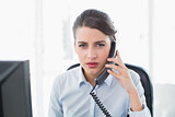 Unsmiling classy brown haired businesswoman answering the telephone