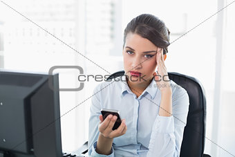 Confused classy brown haired businesswoman holding a mobile phone
