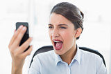 Furious classy brown haired businesswoman yelling at her mobile phone