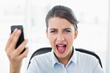 Annoyed classy brown haired businesswoman screaming while holding a mobile phone