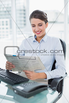 Pleased classy brown haired businesswoman reading a newspaper